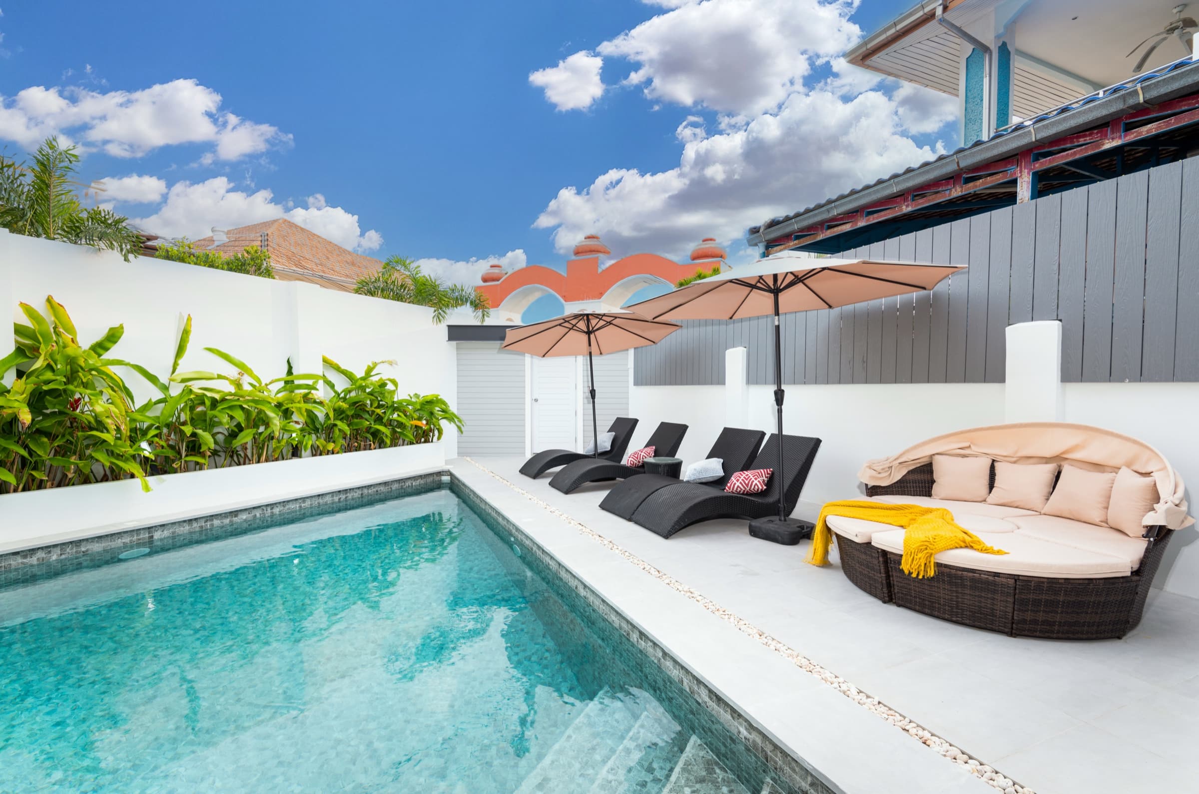 The triangle saltwater pool at Villa Azure — peach umbrellas, sun loungers, and the brown rattan cabana under a clear sky.